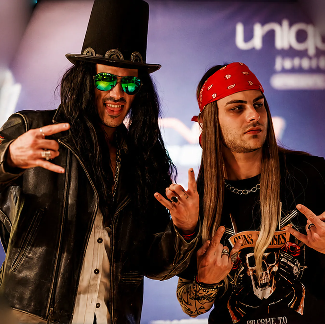 Dois personagens do rock fantasiados, um de cartola e óculos espelhados, outro de bandana vermelha, fazendo o sinal do rock numa edição anterior
