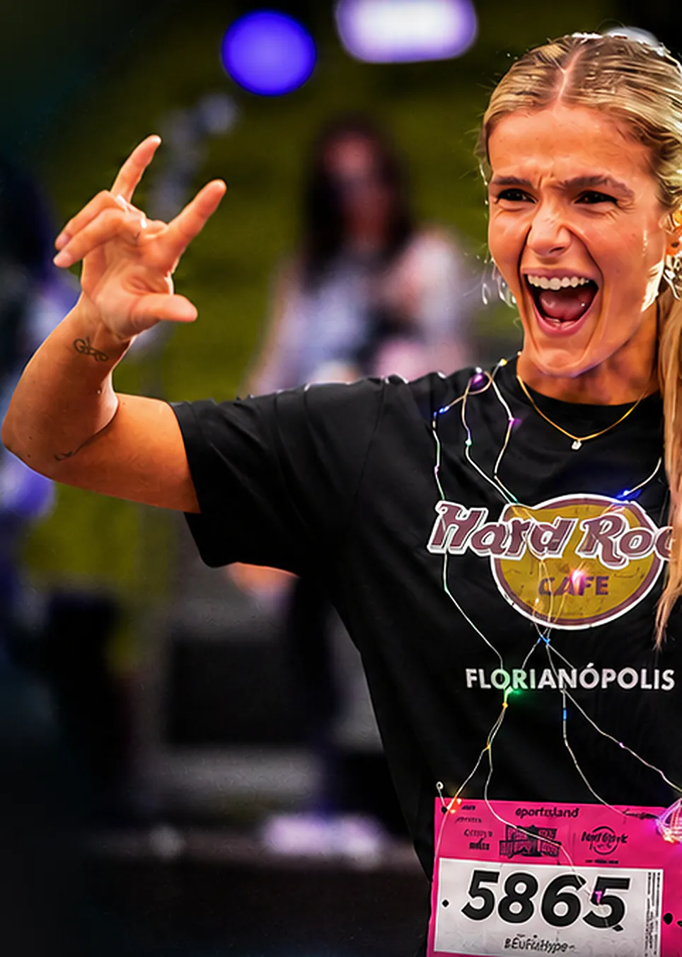 Atleta loira com número de peito gritando e fazendo o sinal do rock durante a Jurerê Night Run