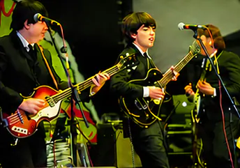 Star Beatles no palco, de terno preto, com guitarras e baixo