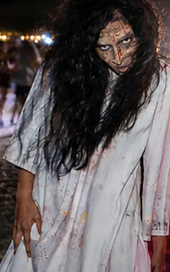 Personagem de terror de vestido branco e cabelo no rosto, na areia