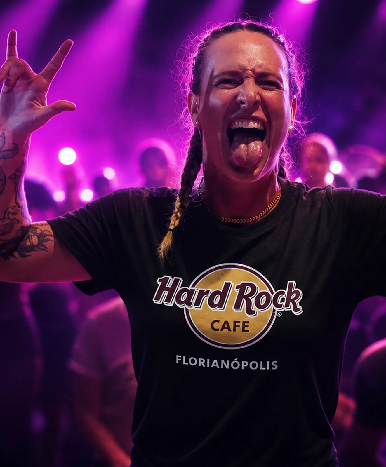 Atleta faz o sinal do rock com a língua de fora sob a luz magenta de um show, com a camiseta do Hard Rock Cafe Florianópolis